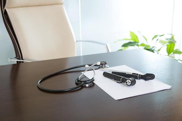A doctor's desk with medical equipment and paper on it