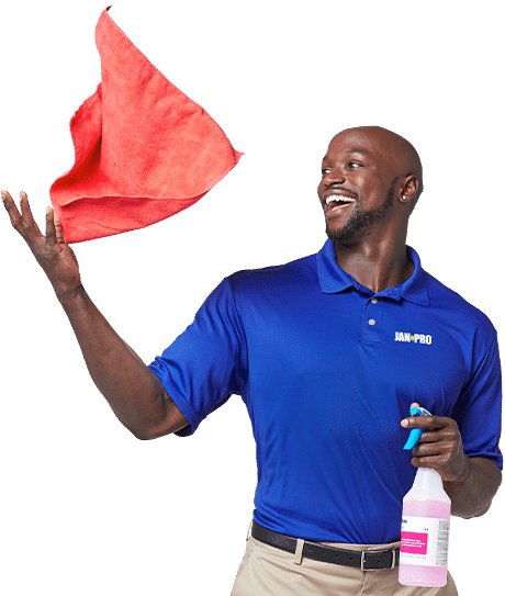 An African-American JAN-PRO Cleaning & Disinfecting employee smiling throwing a red cloth in the air and holding a spray bottle