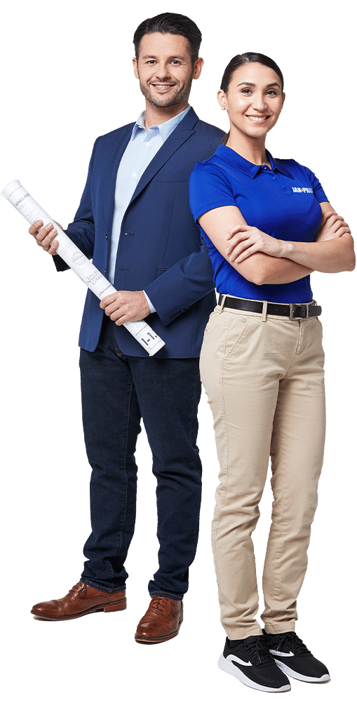 a man in a suit holding a rolled up plans and woman in JAN-PRO Cleaning & Disinfecting attire with her arms folded smiling