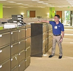 A Caucasian man JAN-PRO Cleaning & Disinfecting employee cleaning a filing cabinet in an office
