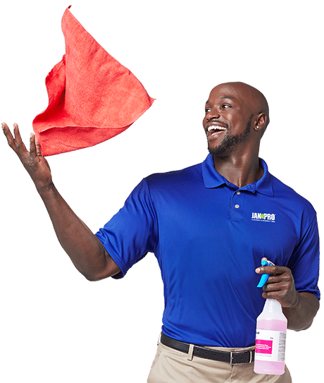 An African-American JAN-PRO Cleaning & Disinfecting employee smiling throwing a red cloth in the air holding a spray bottle