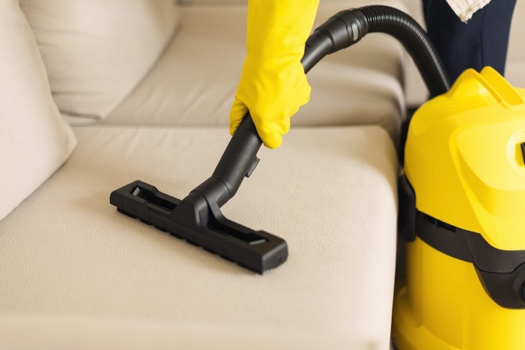Woman cleaning sofa with yellow vacuum cleaner.