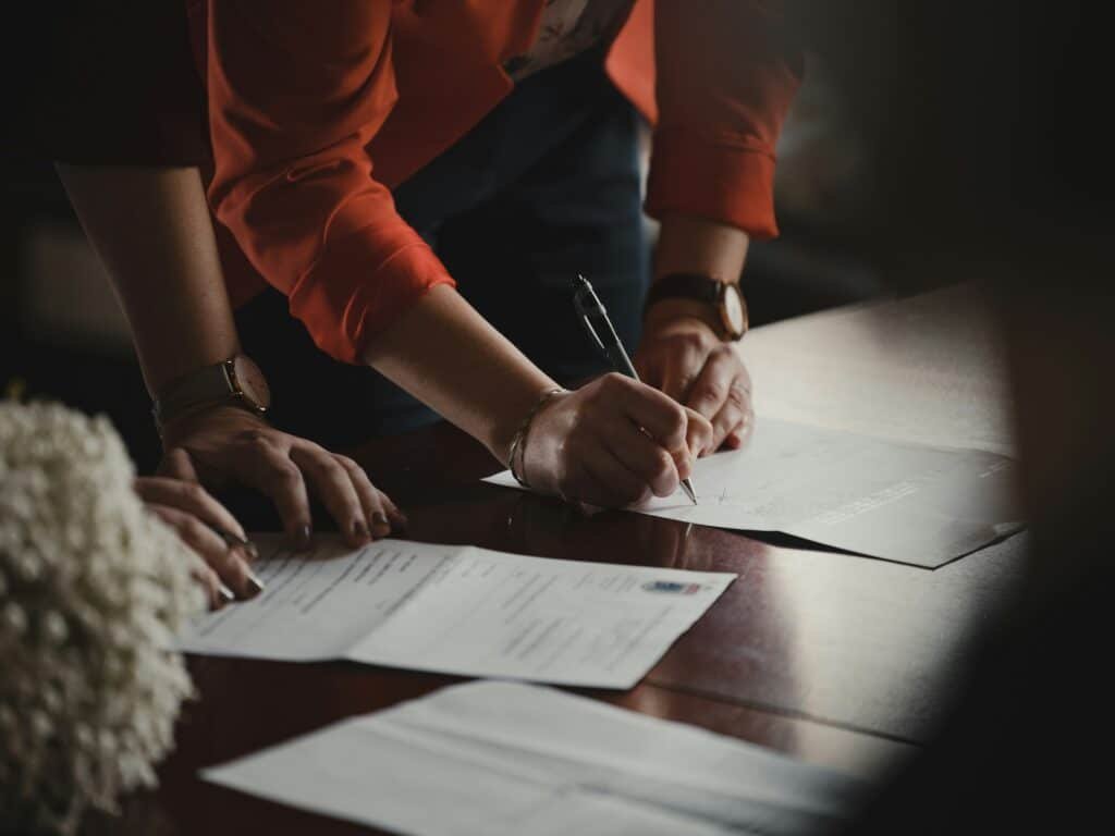 two people looking through and signing documents on a dark brown table