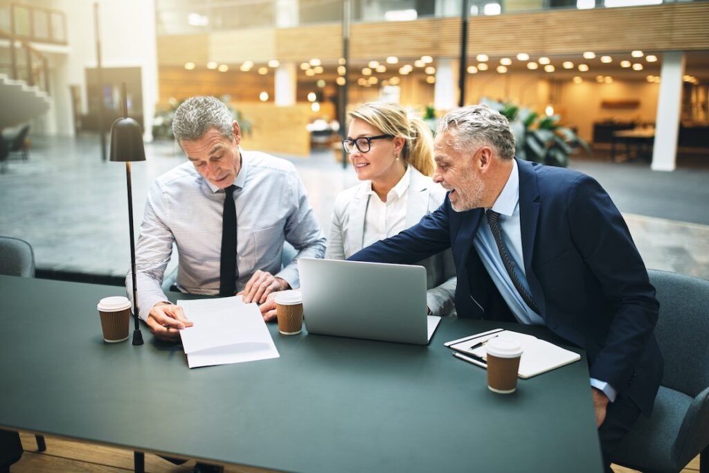 Business people using a laptop and discussing paperwork while having a meeting together in the lobby of an office building.