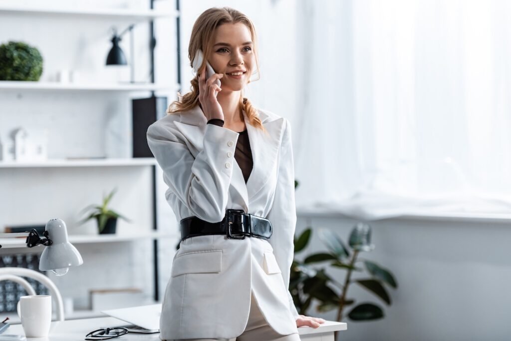 Smiling businesswoman in white formal wear talking on smartphone at workplace
