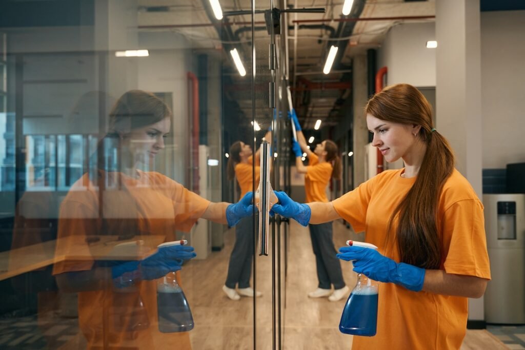 Two young business owners with a commercial cleaning company clean mirrored surfaces of a coworking space.
